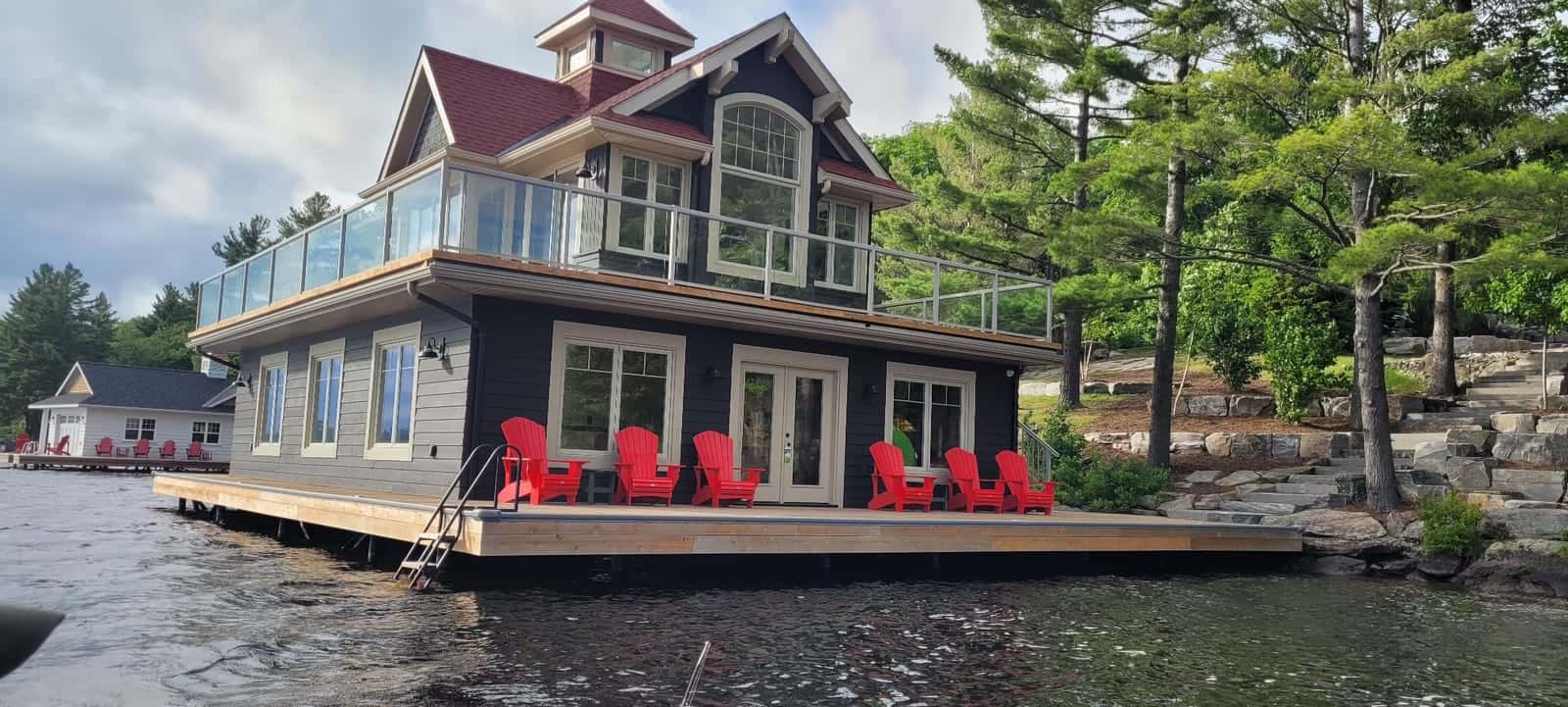 Two-storey boathouse with charcoal siding, red shingle roof, cupola and glass-railed upper deck