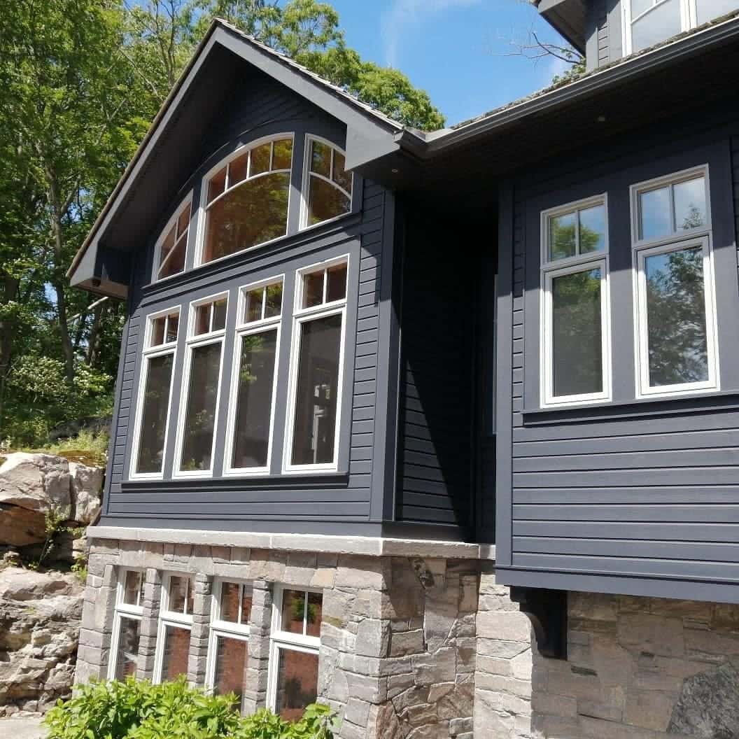 Custom home with near-black siding, an arched gable window and white trim, set on a full stone storey against a granite outcrop