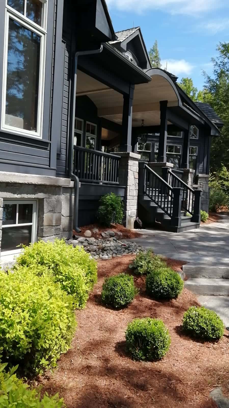 Covered entry porch of a charcoal custom home on stone piers with a curved roof over the door