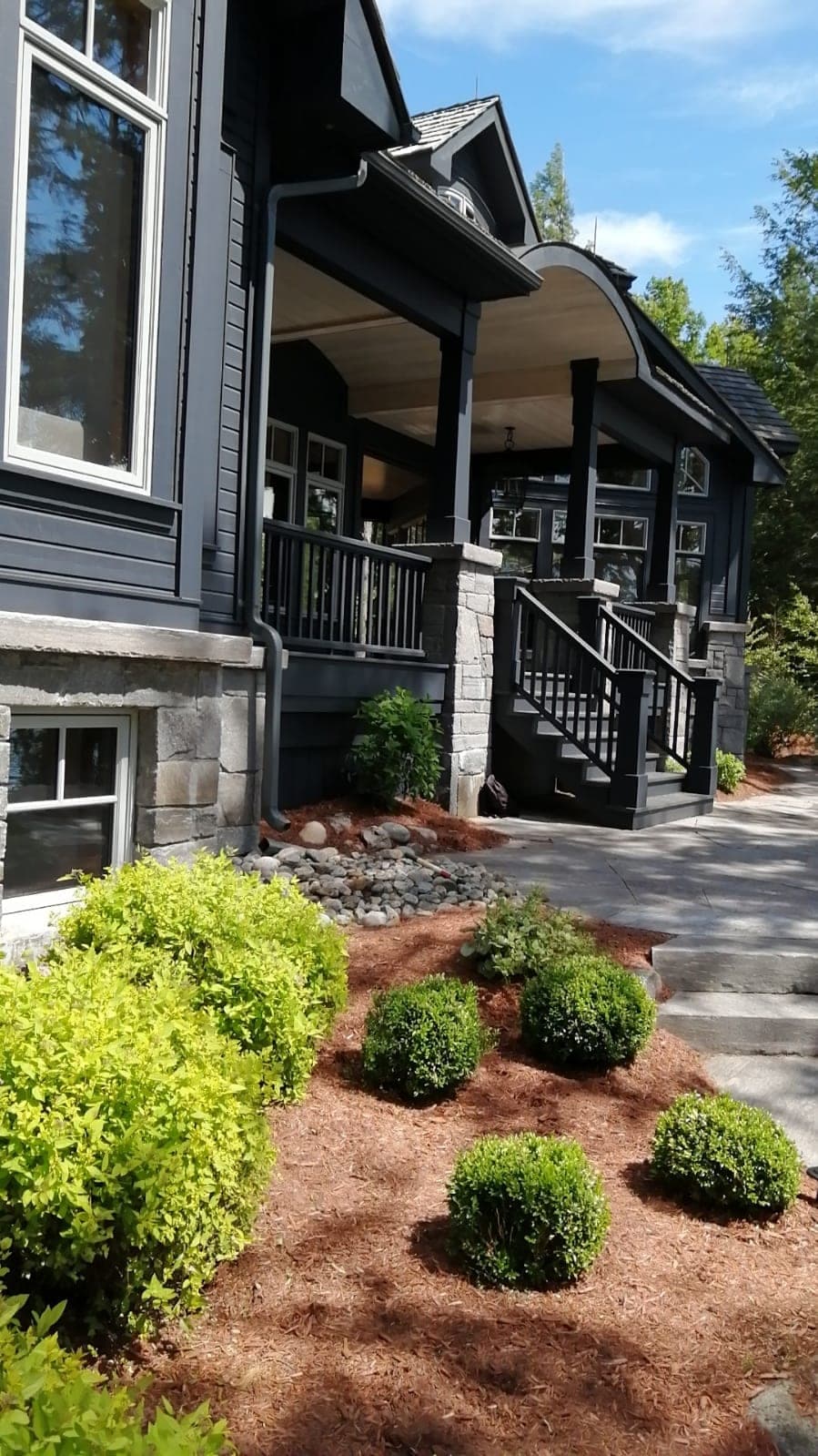 Covered entry porch of a charcoal custom home on stone piers with a curved roof over the door, an Eden Fine Homes build