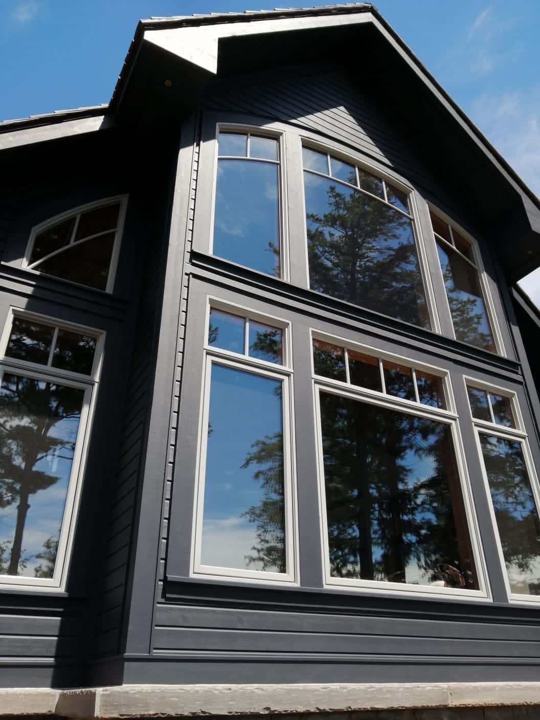 Gable end of a charcoal custom home with tall arched multi-pane windows and white trim