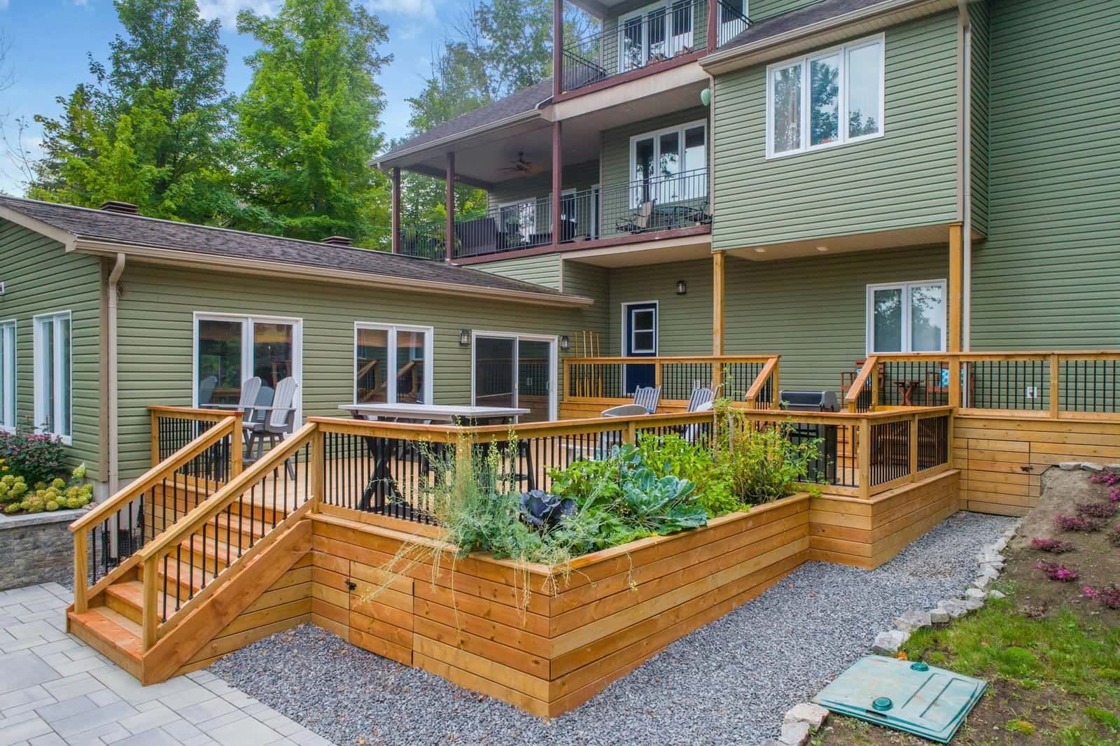 New cedar deck with railings, stairs and built-in raised planters behind a green-sided house