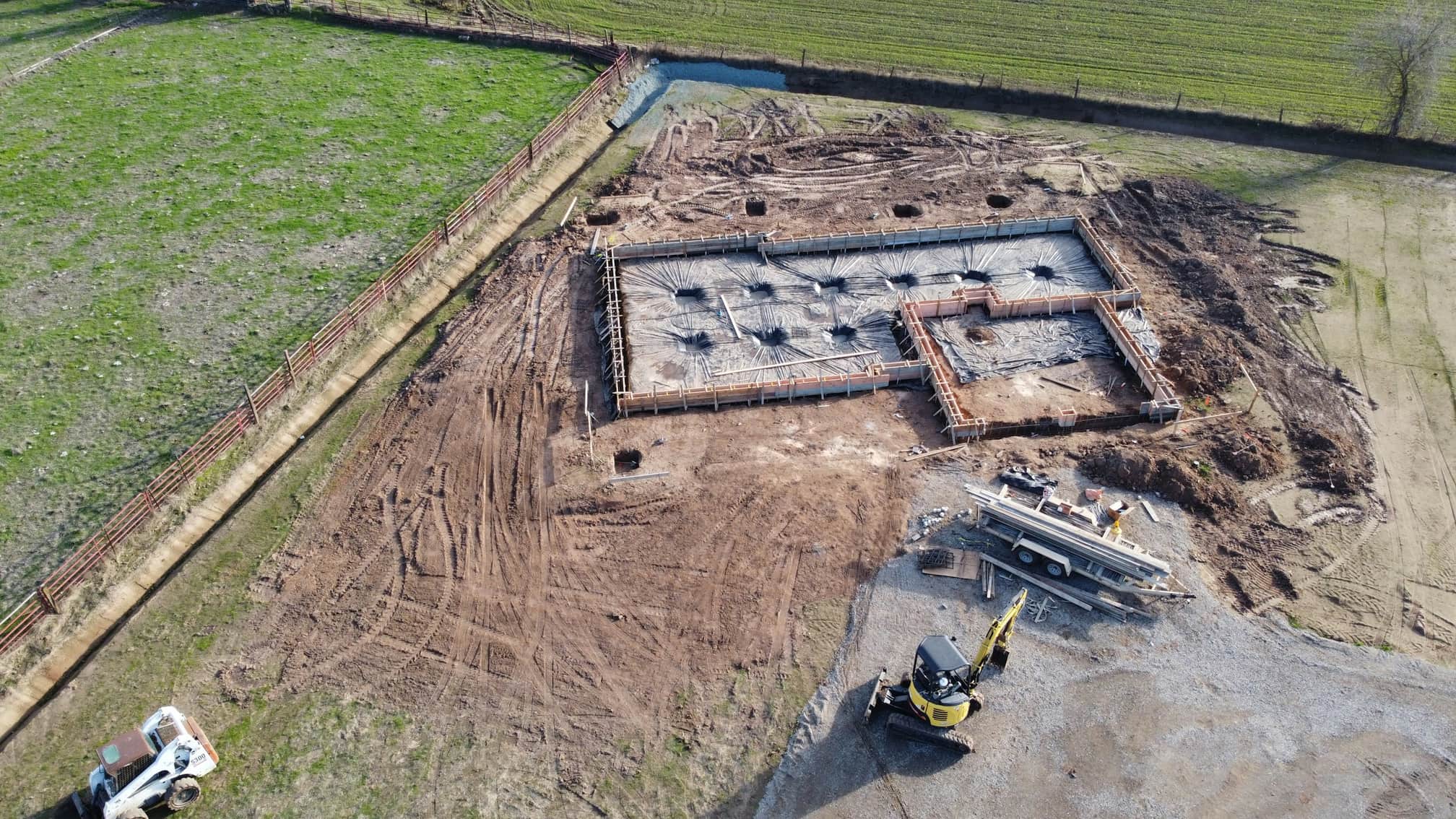 Aerial view of a new foundation with footings poured and formwork in place beside an excavator