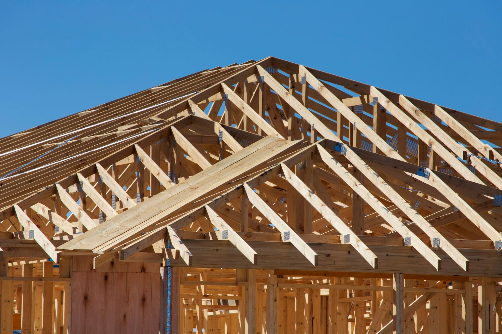 Engineered roof trusses set on a framed house against a clear blue sky