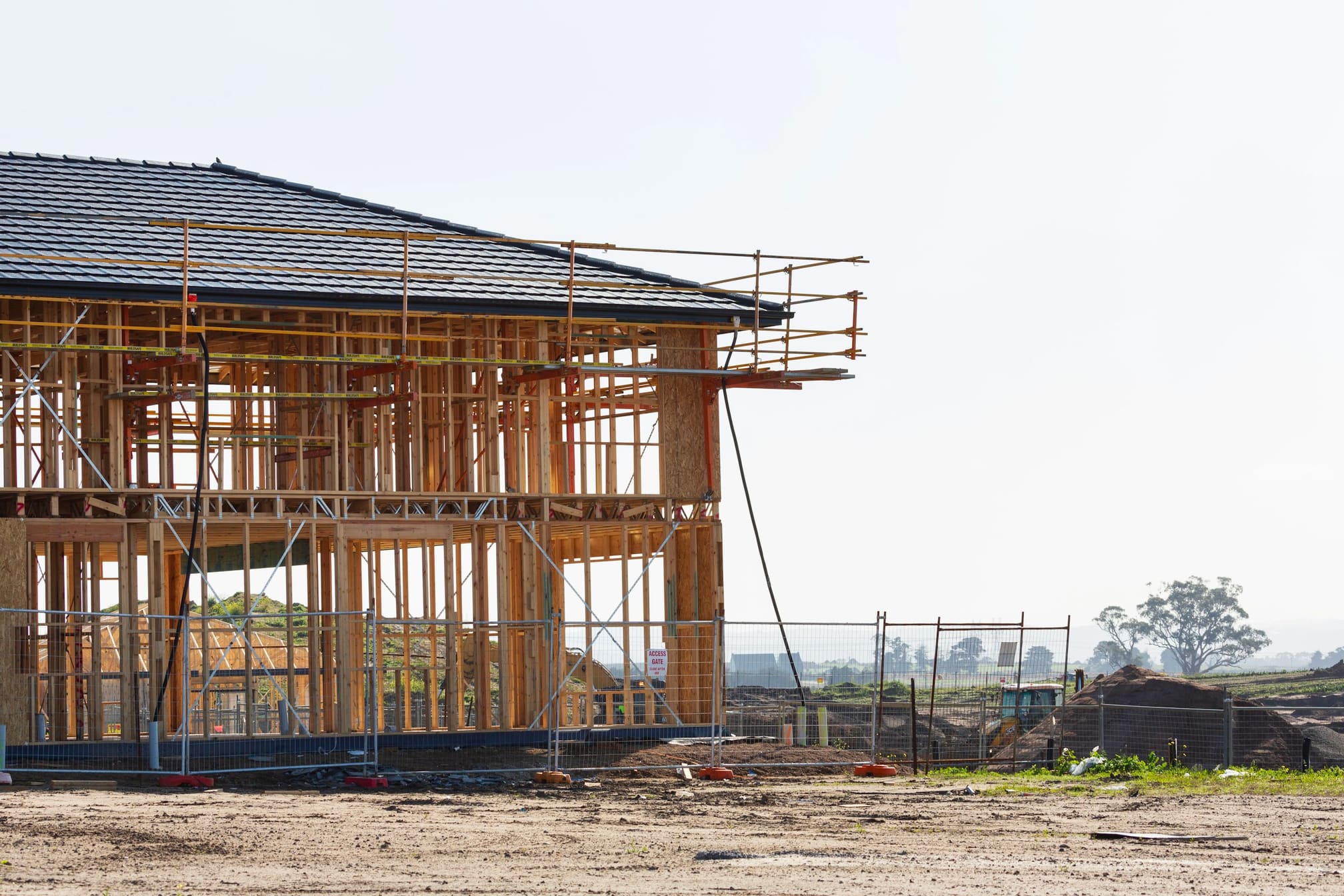 Two-storey house frame with scaffolding along one wall under a clear sky